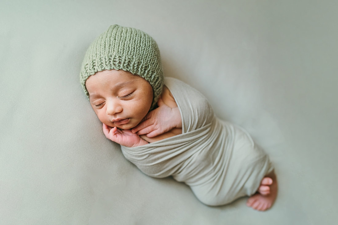 newborn baby boy wearing green knit bonnet wrapped in green blanket for newborn photos in memphis